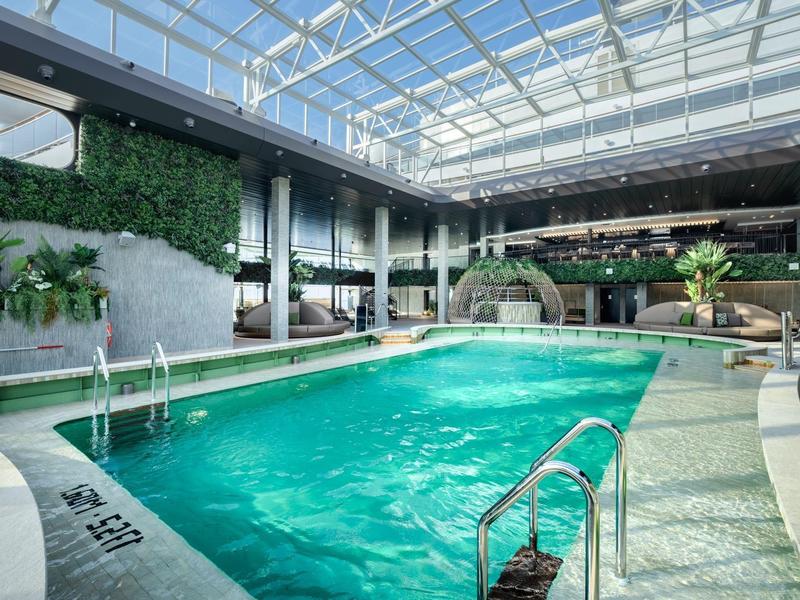 Helles Hallenbad mit Glasdach, grünen Pflanzen und moderner Einrichtung.