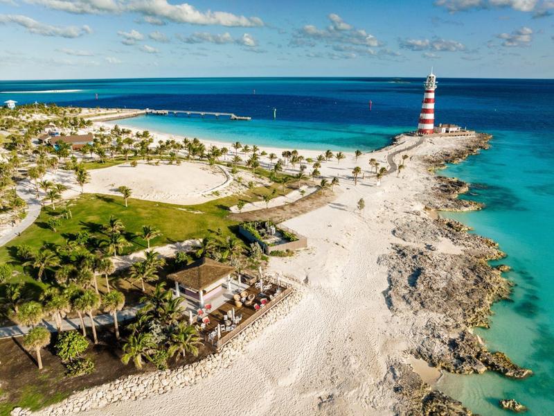 Strand mit Leuchtturm, blauer Himmel und klarem Meerwasser an tropischer Küste.