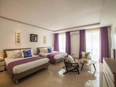 Modernes Hotelzimmer mit zwei Betten, violetten Akzenten und Sitzbereich am Fenster.