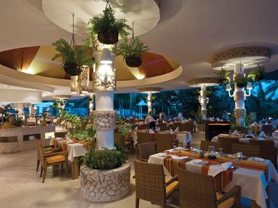 Offenes Restaurant mit gedeckten Tischen und grünen Pflanzen in entspannter Atmosphäre.