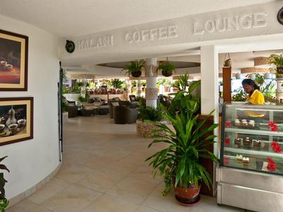 Hell beleuchtete Hotel-Lounge mit Pflanzen, Sofas und einer Vitrine mit Snacks.