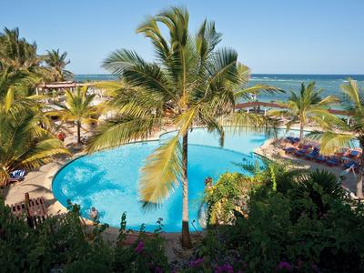 Runder Hotelpool mit Palmen und Sonnenschirmen neben dem Meer unter blauem Himmel.