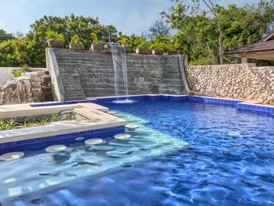 Modernes Schwimmbecken mit Wasserfall und integriertem Whirlpool in einem Gartenbereich.