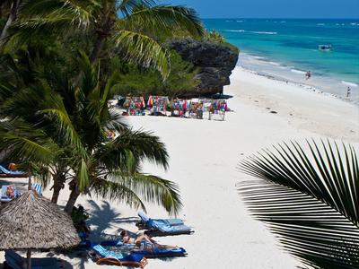 Weißer Sandstrand mit Liegestühlen, Palmen und klarem blauem Meer unter blauem Himmel.