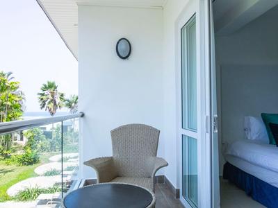 Balkon mit Stuhl, Tisch und Blick auf Garten und Palmen neben einem Schlafzimmer.