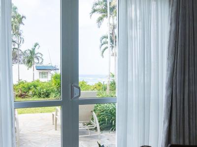 Heller Wohnraum mit Glastür, die auf eine Terrasse mit Palmen und Garten öffnet.