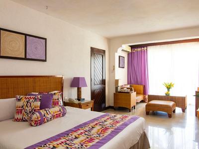 Helles Hotelzimmer mit Doppelbett, lila Akzenten und großem Fenster mit Vorhängen.