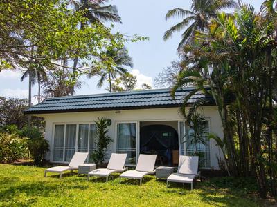 Kleines Hotelgebäude mit Sonnenliegen und üppigem tropischen Garten bei Sonnenschein.