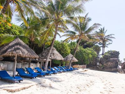 Sandstrand mit blauen Liegestühlen und Palmen neben Strohdachhütten am Hotelstrand.