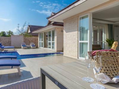 Moderne Terrasse mit Pool, Sonnenliegen und Getränke auf einem Tisch vor einem Haus.
