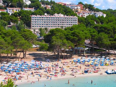 Beach with many colorful umbrellas and a hotel building in the background.