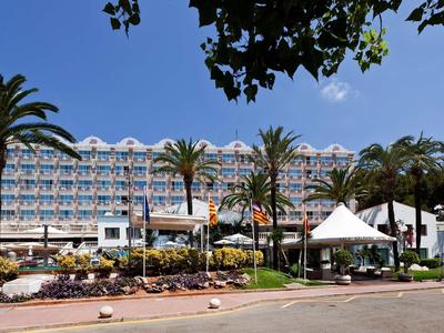 Multi-story hotel building surrounded by palm trees and flower beds in the foreground