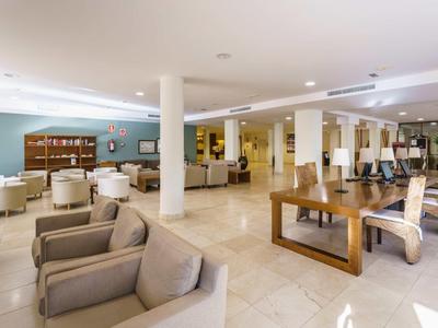 Bright, modern lounge area with sofas, armchairs, and tables in a hotel.