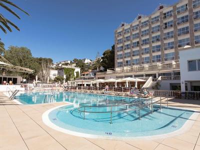 Large outdoor pool in front of multi-story hotel with lounge chairs and clear sky.