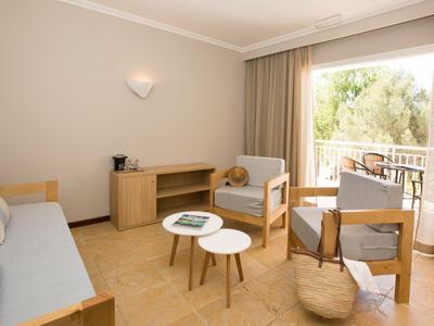 Hell eingerichtetes Hotelzimmer mit Sofa, Sesseln und kleinem Couchtisch vor einem Balkon.