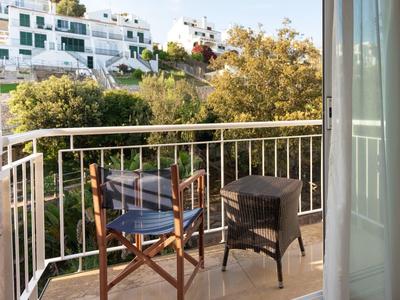 Balkon mit Holzstuhl und kleinem Tisch mit Blick auf Bäume und angrenzende Gebäude