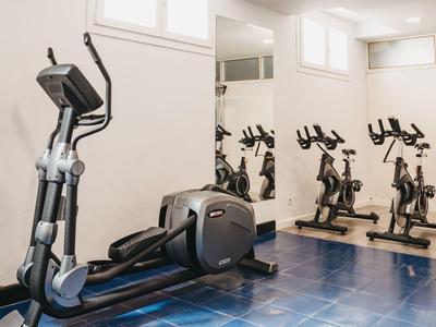 Kleiner Fitnessraum mit Ellipsentrainer und zwei Fahrrädern vor Spiegelwand