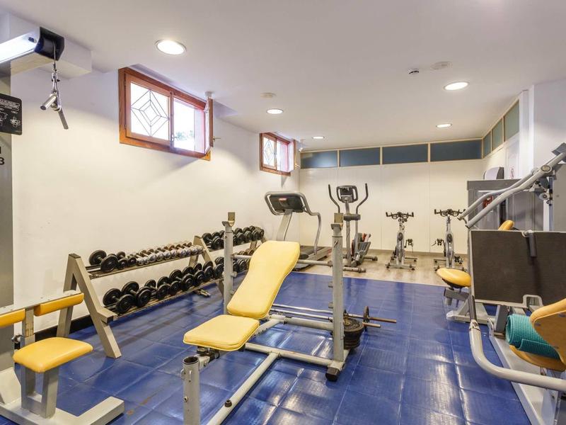 Modern gym with equipment and dumbbells in a bright room with blue floor tiles.