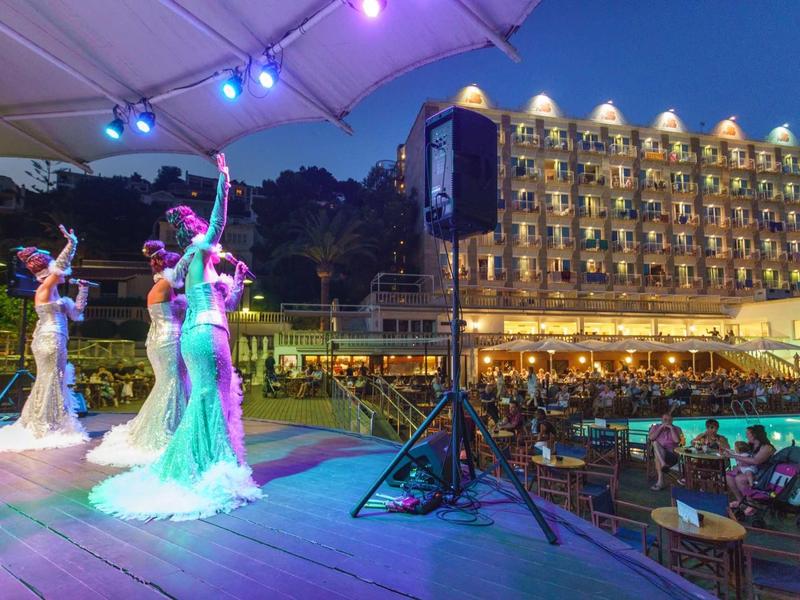 Dancers in colorful dresses performing on a stage during an evening show in front of a lit hotel.