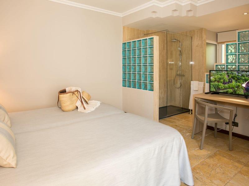 Helles Hotelzimmer mit Doppelbett, Schreibtisch und Blick auf eine Duschkabine mit Glasbausteinen.