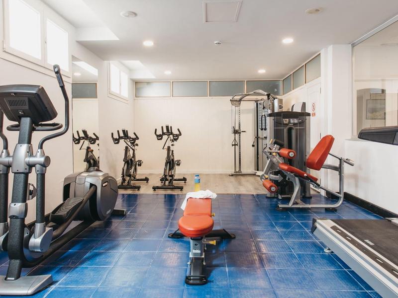 Hell erleuchteter Fitnessraum mit verschiedenen Trainingsgeräten und blauem Boden