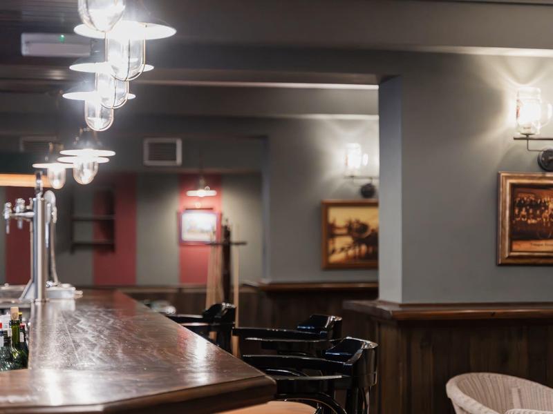 Gemütliche Hotelbar mit Holztresen, Stühlen und gedämpfter Beleuchtung an der Decke.