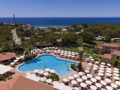Grande piscina dell'hotel con lettini e ombrelloni, circondata da verde e vista mare.