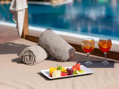 Due Aperol Spritz, piatto di frutta e asciugamani vicino alla piscina di un hotel.