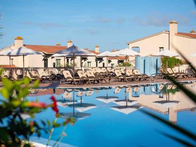 Hotel con piscina all'aperto e lettini sotto gli ombrelloni in una giornata di sole.
