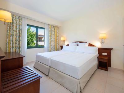 Camera d'albergo luminosa con due letti, comodini, lampada e finestra con tende.