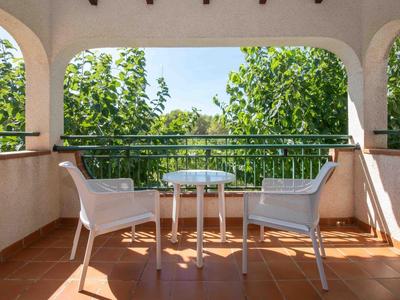 Balcone con due sedie bianche e un piccolo tavolo rotondo davanti ad alberi verdi sotto un cielo limpido.