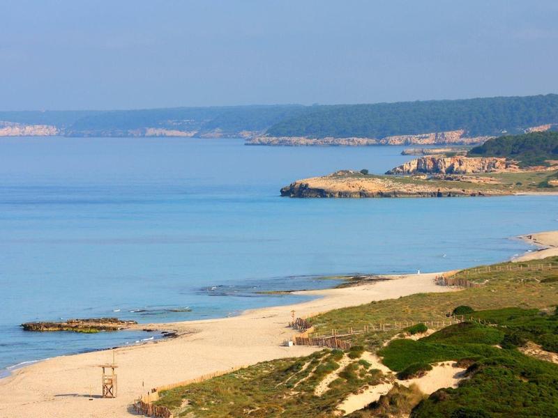 Ampia costa sabbiosa con mare blu e colline boscose sullo sfondo