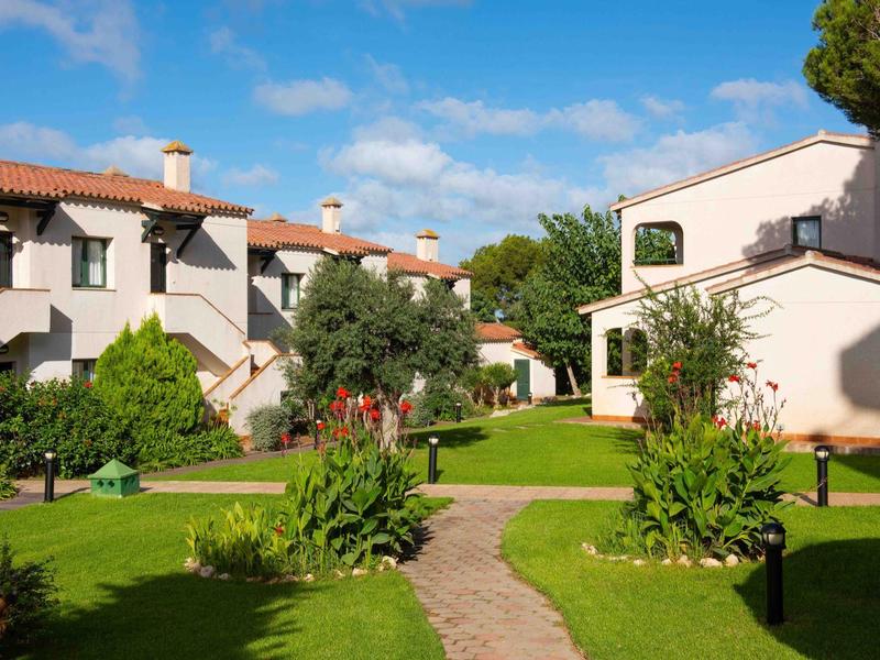 Sentiero tra case con tetti rossi in un giardino curato sotto un cielo soleggiato