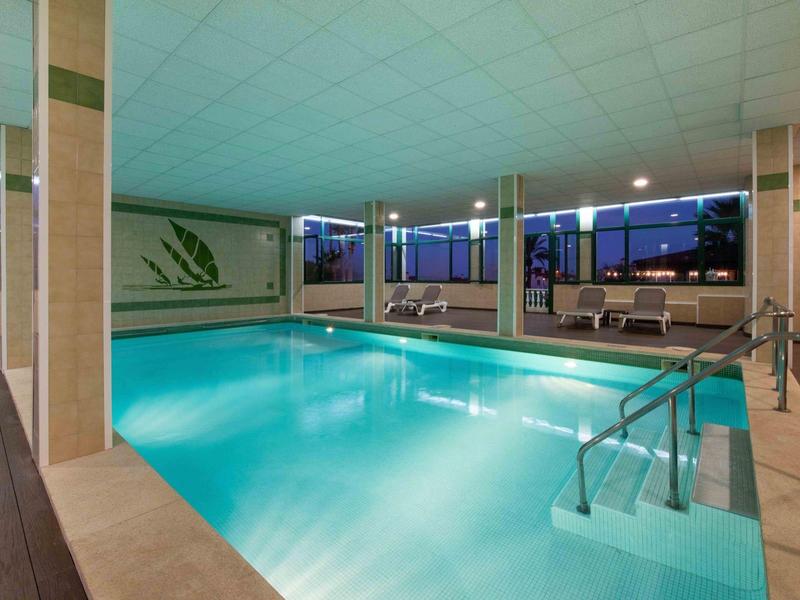 Piscina coperta riscaldata con posti a sedere e grandi finestre al crepuscolo.