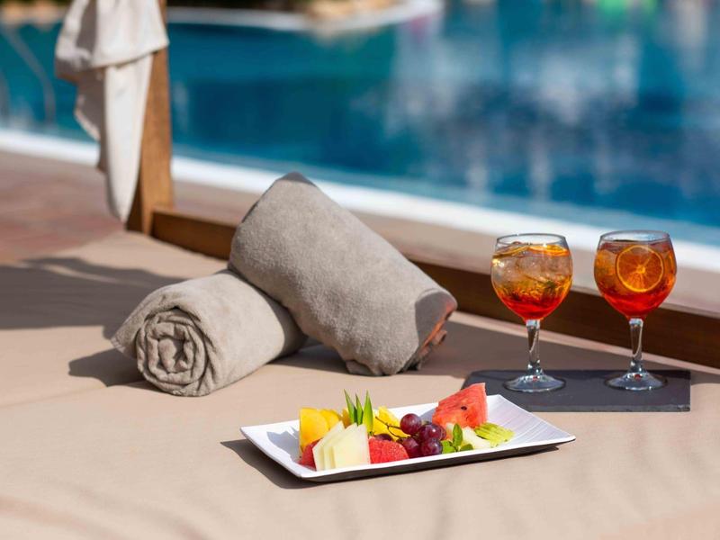 Due Aperol Spritz, piatto di frutta e asciugamani vicino alla piscina di un hotel.