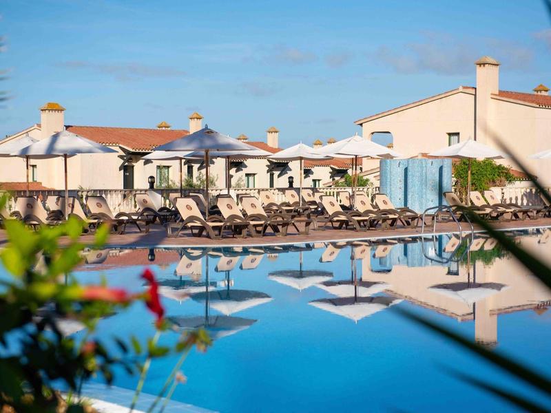 Hotel con piscina all'aperto e lettini sotto gli ombrelloni in una giornata di sole.