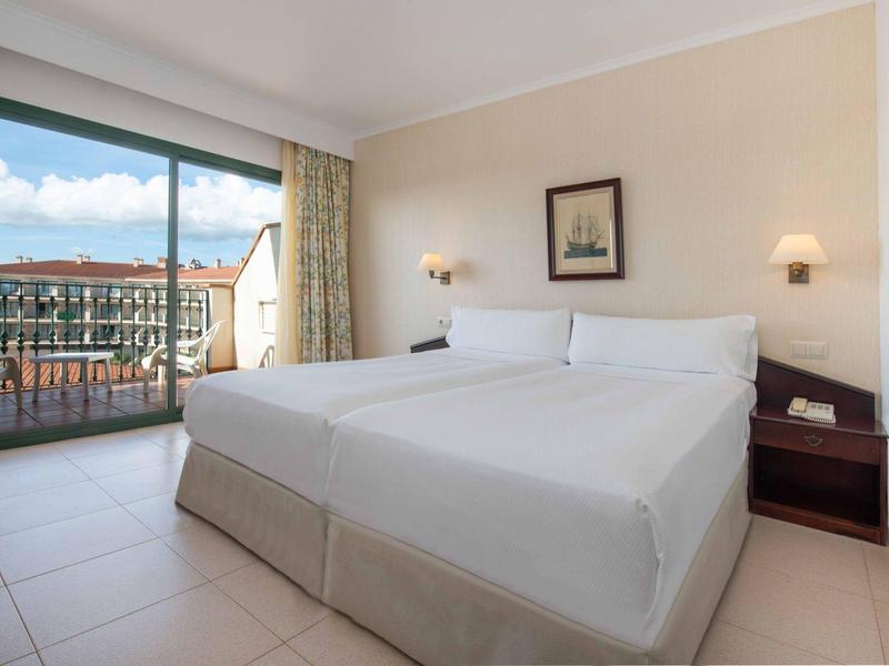 Camera d'hotel luminosa con letto matrimoniale e balcone con vista sulla città.