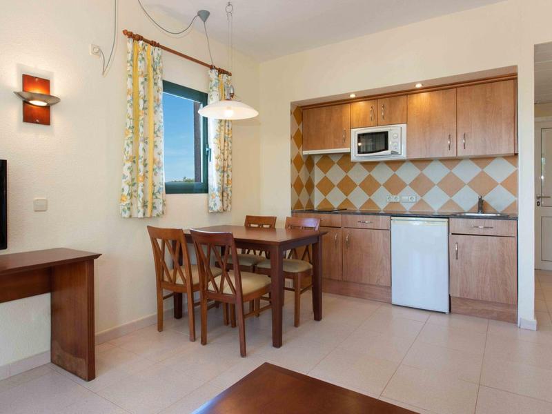 Angolo pranzo accogliente con sedie in legno, mobili da cucina, microonde e piccolo frigorifero in un appartamento per vacanze.