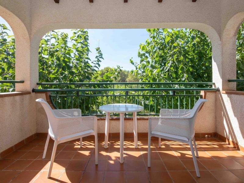 Balcone con due sedie bianche e un piccolo tavolo rotondo davanti ad alberi verdi sotto un cielo limpido.