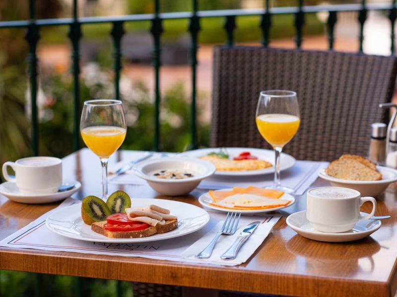 Tavolo per la colazione su una terrazza con succo, caffè, frutta e dolci.