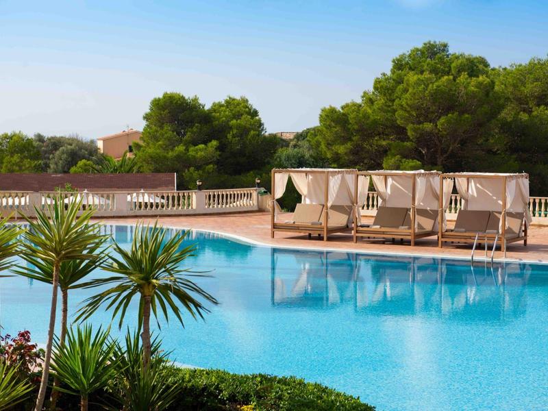Grande piscina all'aperto con lettini e vegetazione in una giornata di sole.
