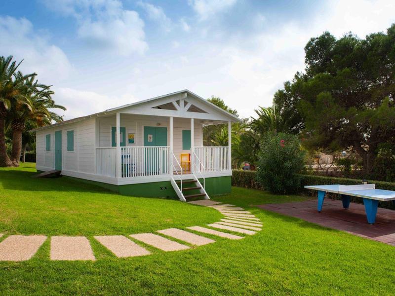 Una casa bianca con veranda e giardino curato con tavolo da ping pong sotto un cielo blu.