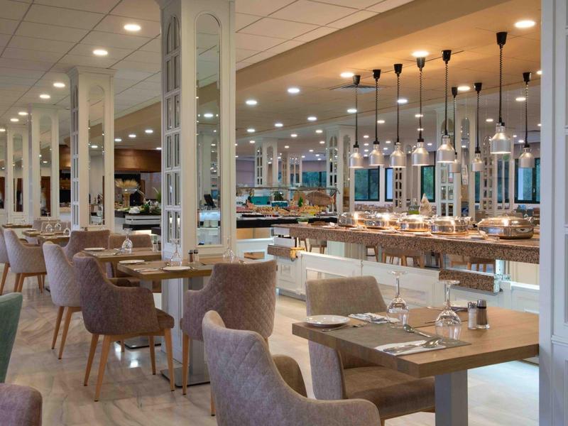 Area ristorante di un hotel moderno con tavoli in legno, poltrone accoglienti e illuminazione elegante.