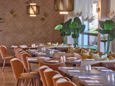 Nowoczesna, jasna restauracja z ciepłymi drewnianymi tonami i pomarańczowymi krzesłami.