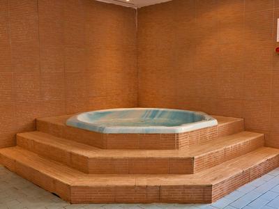 Sześciokątny jacuzzi w prostym, brązowo wyłożonym płytkami pomieszczeniu z schodami.