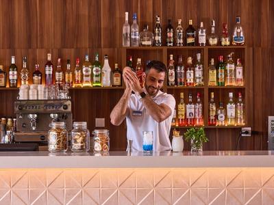 Barman miesza drinka za barem z drewnianymi półkami i butelkami alkoholu.