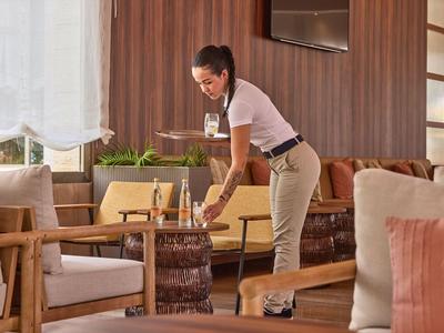 Pracownik hotelu sprząta stół w przytulnym, nowoczesnym salonie z drewnianymi meblami.
