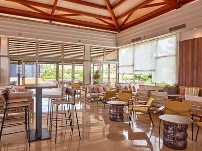 Jasny salon hotelowy z drewnianym sufitem, dużymi oknami i wygodnymi miejscami do siedzenia.