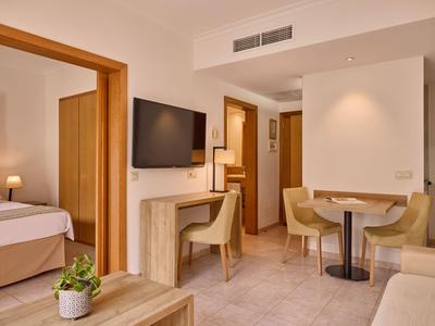 Nowocześnie urządzony pokój hotelowy z częścią wypoczynkową, stołem, krzesłami i telewizorem.