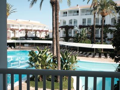 Uitzicht op hotelzwembad met palmbomen en ligstoelen op een zonnige dag.